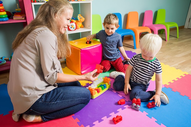 Foto twee kleine jongens spelen met een kleuterjuf de vrouw zit met jongens op de grond in de speelkamer