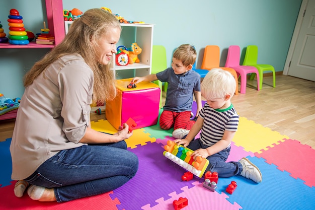 Twee kleine jongens spelen met een kleuterjuf De vrouw zit met jongens op de grond in de speelkamer