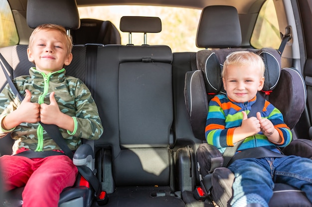 Twee kleine jongens zittend op een autostoeltje en een stoelverhoger vastgemaakt in de auto.