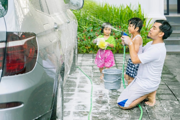 Twee kleine kinderen helpen hun vader met het wassen van een auto