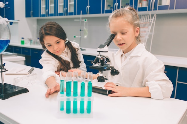 Twee kleine kinderen in laboratoriumjas het leren van chemie in schoollaboratorium. Jonge wetenschappers die in beschermende bril experimenteren in laboratorium of chemisch kabinet. Kijkend door de microscoop