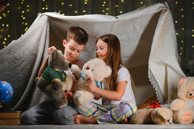 Twee kleine kinderen spelen 's avonds thuis om een kampeertent te bouwen om met een zaklamp boeken te lezen en binnen te slapen. Begrip: spel, magie, creativiteit, alarmsystemen