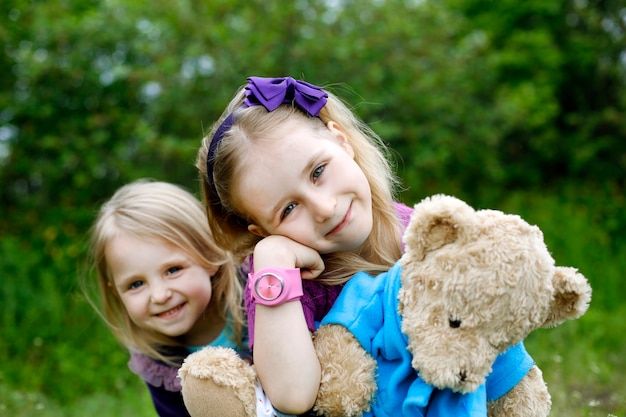 Twee kleine meisjes broers en zussen knuffelen teddybeer in de natuur