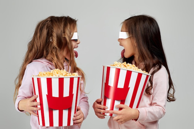 Twee kleine meisjes die in roodblauwe 3d glazen emmers popcorn houden