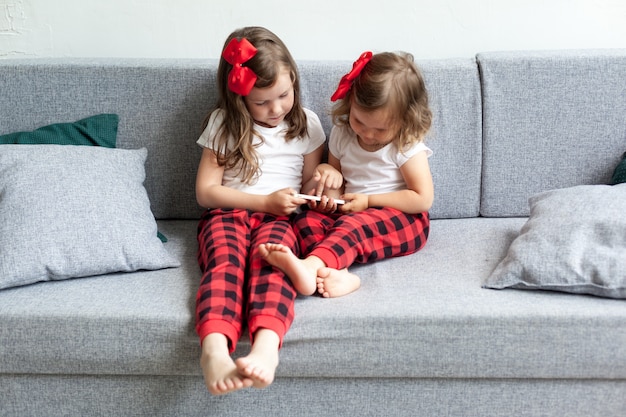 Twee kleine meisjes die op bank zitten en op smartphone spelen.