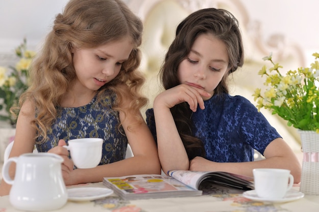 Twee kleine meisjes die thee drinken en een tijdschrift lezen