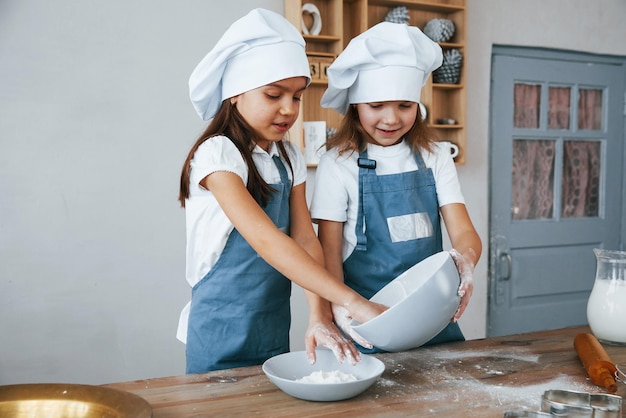 Twee kleine meisjes in blauw chef-kokuniform die met bloem aan de keuken werken