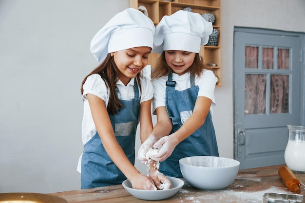 Twee kleine meisjes in blauw chef-kokuniform die met bloem aan de keuken werken