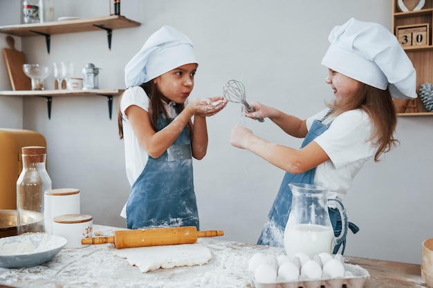 Twee kleine meisjes in blauw chef-kokuniform die plezier hebben en eten bereiden in de keuken