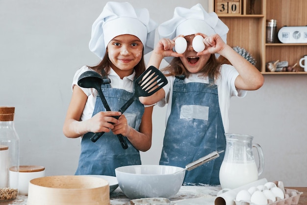 Twee kleine meisjes in blauw chef-kokuniform hebben plezier tijdens het bereiden van voedsel in de keuken