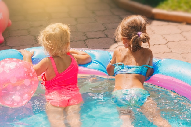 twee kleine meisjes in zwemkleding spelen in het kinderzwembad in de tuin