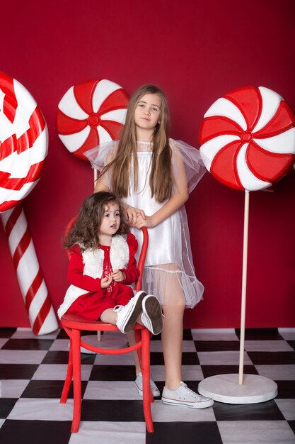 Twee kleine meisjes met grote kerstsnoepjes op een geïsoleerde rode achtergrond