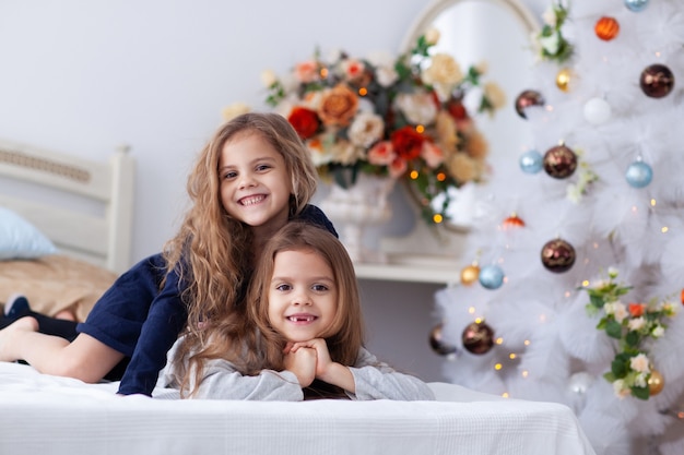 Twee kleine meisjes op een bed en een kerstboom