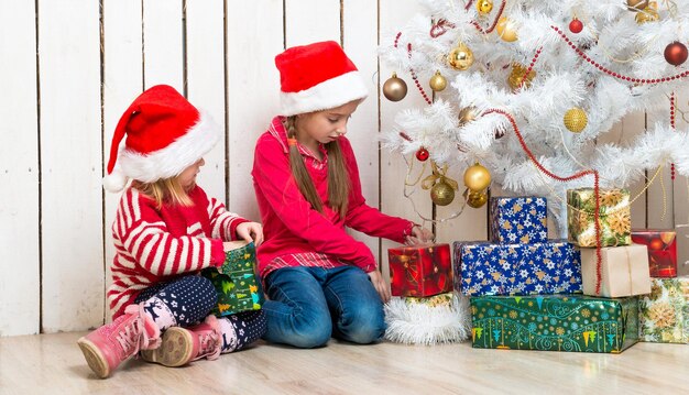 Twee kleine meisjes openen kerstcadeaus op de vloer.