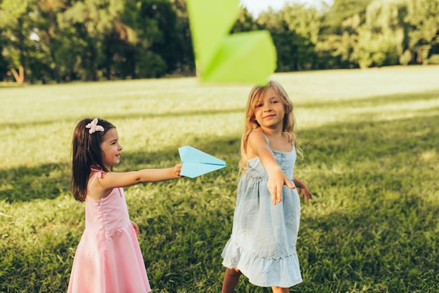 Twee kleine meisjes spelen met een papieren vliegtuigje in een zomerdag in het park Schattige kinderen gooien vliegtuigen buiten in de tuin Jeugdconcept