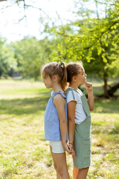 Twee kleine meisjes staan rug aan rug in het park