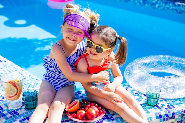 twee kleine meisjes zitten in de zomer bij het zwembad met een zonnebril en limonade drinken