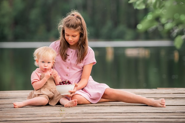 Twee kleine meisjeszusters eten kersen in de natuur op het platteland Gezonde voeding