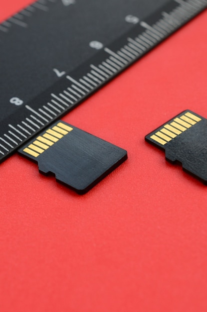 Twee kleine micro SD-geheugenkaarten liggen op een rode achtergrond naast een zwarte liniaal