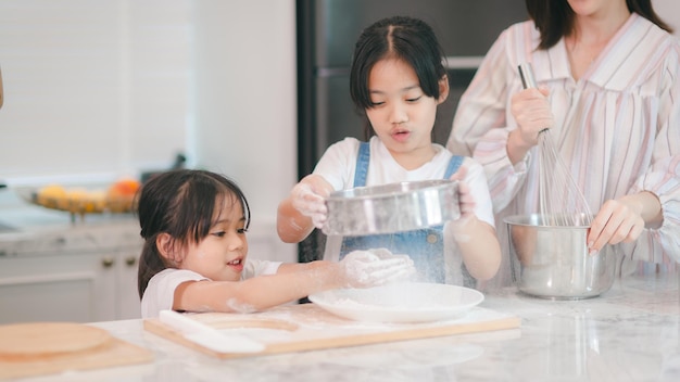 Twee kleine schattige Aziatische meisjes leren hoe ze brood en bakkerij moeten maken met een nieuwsgierig en blij lachend gezicht. Ze leert en speelt