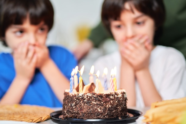 Twee kleine Spaanse tweelingen kijken naar verjaardagstaart, maken wensen terwijl ze zich voorbereiden op het uitblazen van kaarsen. Latijnse familie die verjaardag samen thuis viert. Selectieve focus op een taart