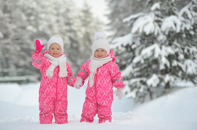 Twee kleine tweelingmeisjes in rode pakken staan in een besneeuwd winterbos.