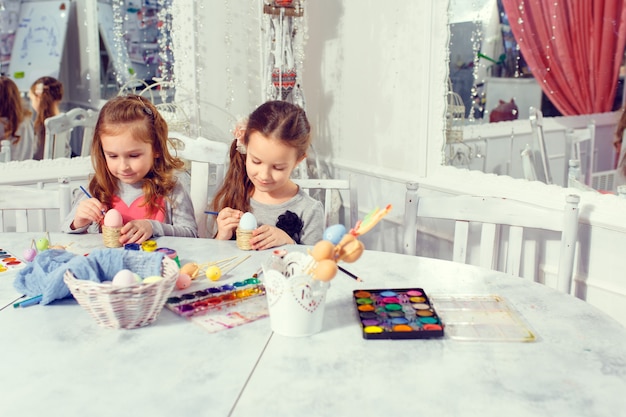 Twee kleine zusters die kleurrijke paaseieren thuis schilderen