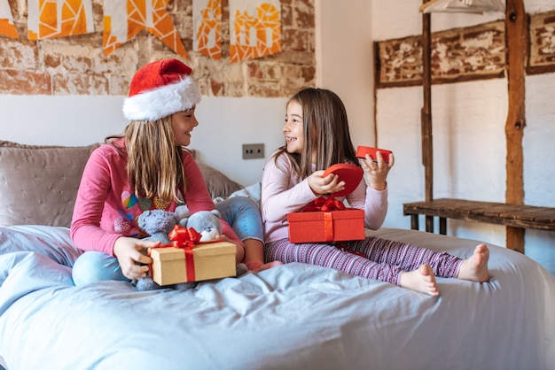 Twee kleine zusters die met elkaar in bed spelen die thuis aanwezige Kerstmis openen