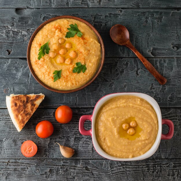 Twee kommen met verse hummus en tomaten op een houten tafel