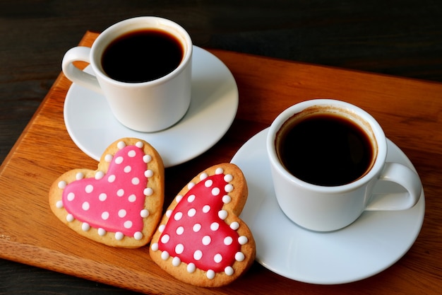 Twee kopjes koffie en gestippelde hartvormige royal icing cookies op houten snijplank