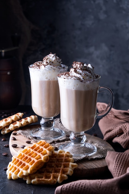 Twee kopjes koffie met slagroom en geraspte chocolade op een donkere betonnen achtergrond. Weense koffie met Weense wafels.