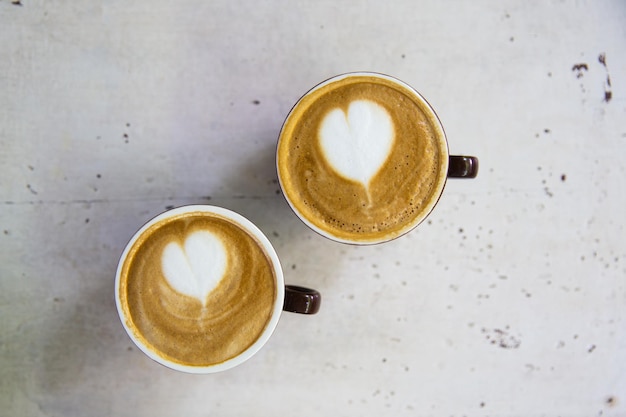 Twee kopjes lekkere cappucino met liefdeskunst latte. Valentijnsdag concept. Witte getextureerde houten tafel achtergrond.