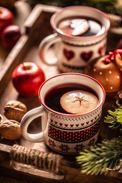 Twee kopjes met warme kerstpunch gekookt van rode wijn rum en vers fruit op smaak gebracht met kruidnagel en kaneel