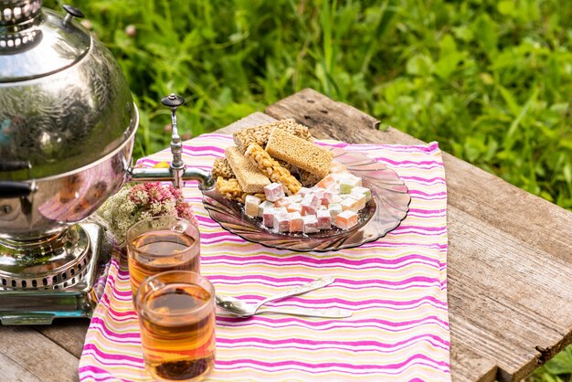 Twee kopjes thee en een samowar op een houten tafel met diverse zoetigheden