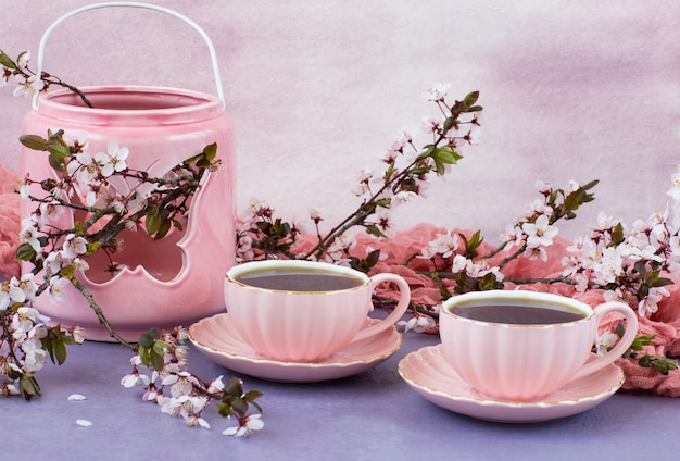 twee kopjes thee in roze schotels en kersenbloesems in een vaas