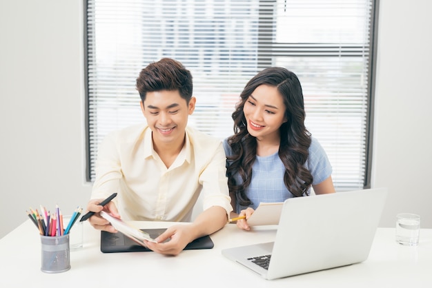 Twee lachende casual ontwerpers die met laptop werken terwijl ze aan een bureau op kantoor zitten