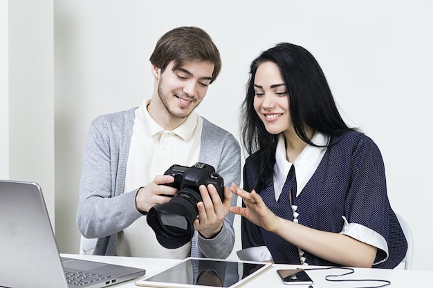 Twee lachende casual ontwerpers man en vrouw werken met laptop en tablet op kantoor. foto's op camera bekijken