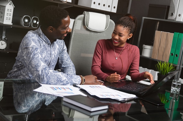 Twee lachende jonge zwarte mensen hebben pret die hun bedrijfszitting bespreken bij Bureau in bureau