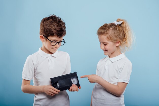 Twee lachende kind jongen en meisje met videoband geïsoleerd op blauwe achtergrond oude gadgets