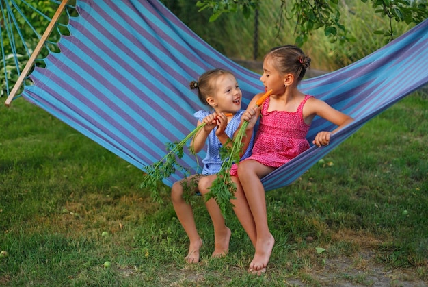 Twee lachende kinderen eten verse wortels op een hangmat.