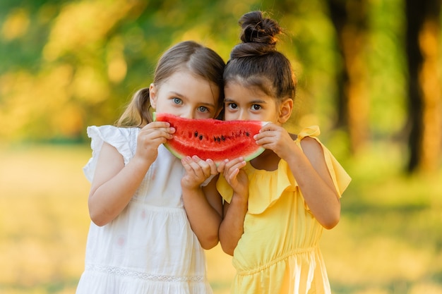 Twee lachende meisjes houden een stuk watermeloen in hun handen Kinderen eten buiten fruit