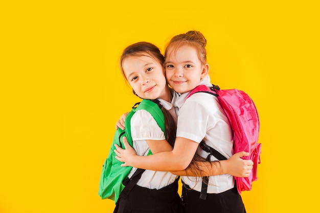 Twee lachende schoolmeisjes in uniform knuffelen naar de gele