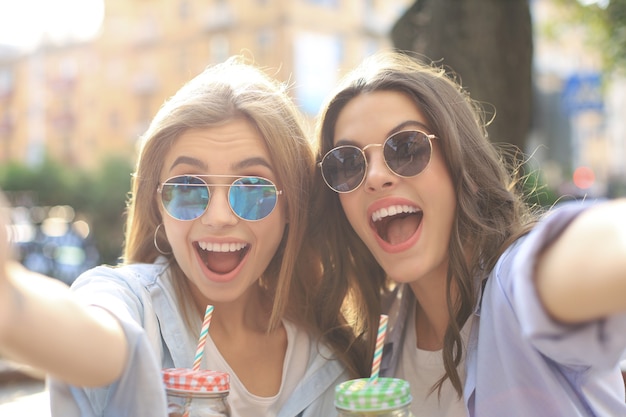 Twee lachende vrienden die samen van het weekend genieten en selfie maken op de achtergrond van de stad.