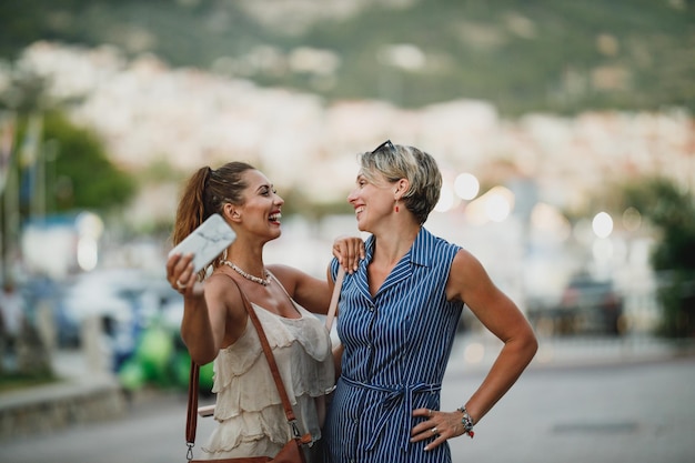 Twee lachende vrouwen hebben plezier en genieten in de zomerdag terwijl ze langs de straat van een mediterrane stad wandelen.