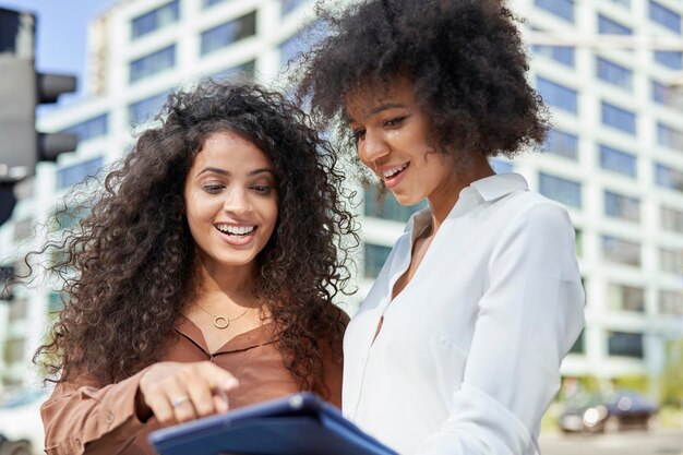 Twee lachende zakenvrouwen met digitale tablet in de stad