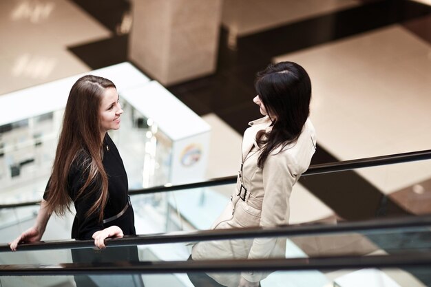 Twee lachende zakenvrouwen staan op een roltrap in een zakencentrum. bedrijfsconcept