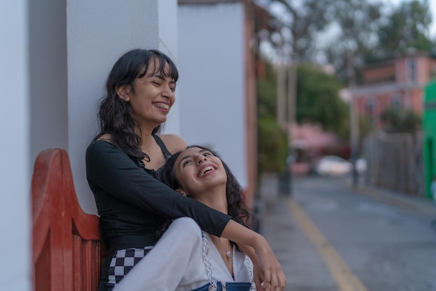 Twee latina-vrienden lachen terwijl ze elkaar omhelzen op straat