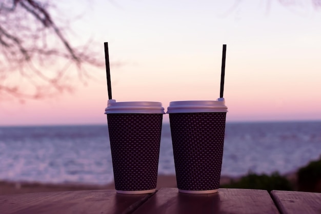 Twee lattes staan op een tafel op het strand. Aan de achterkant zie je de zonsondergang. Hoge kwaliteit foto