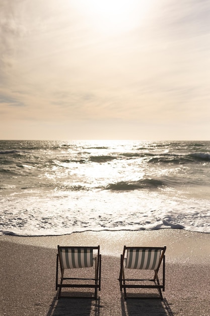 Foto twee lege opvouwbare houten stoelen aan de kust voor golven die in zee spatten op het strand tegen de hemel