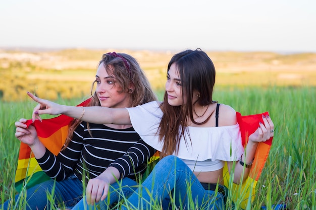 Twee lesbische meisjes liggend op het gras met de gay pride-vlag